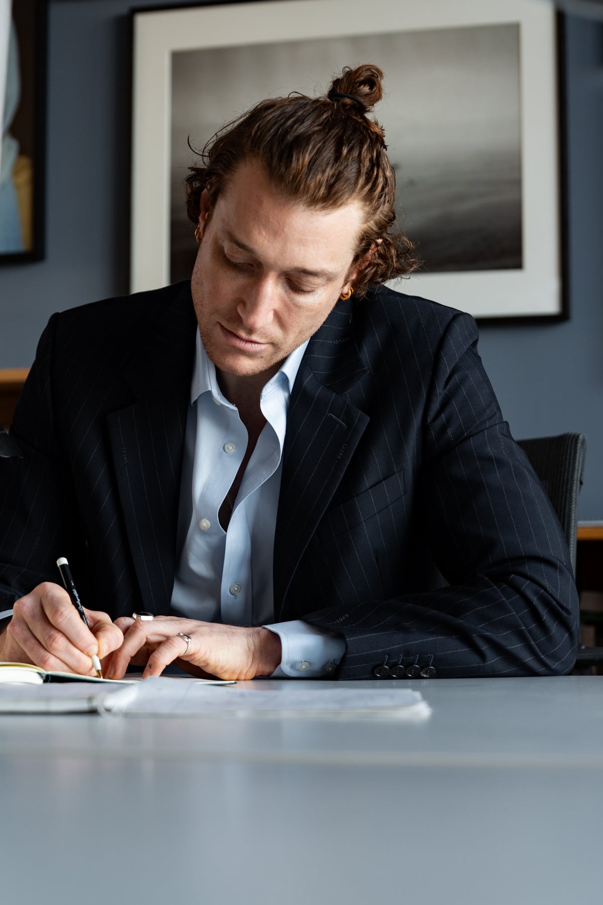 Man in a suit writing at a desk with a framed picture in the background