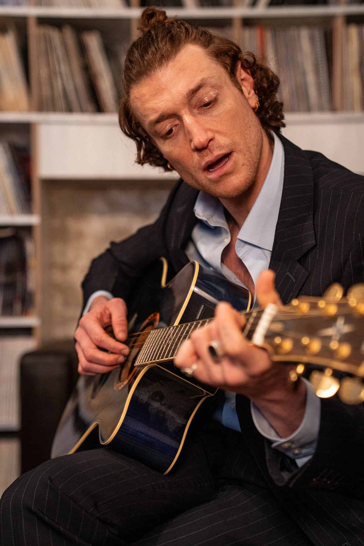 Man playing guitar in a room with bookshelves