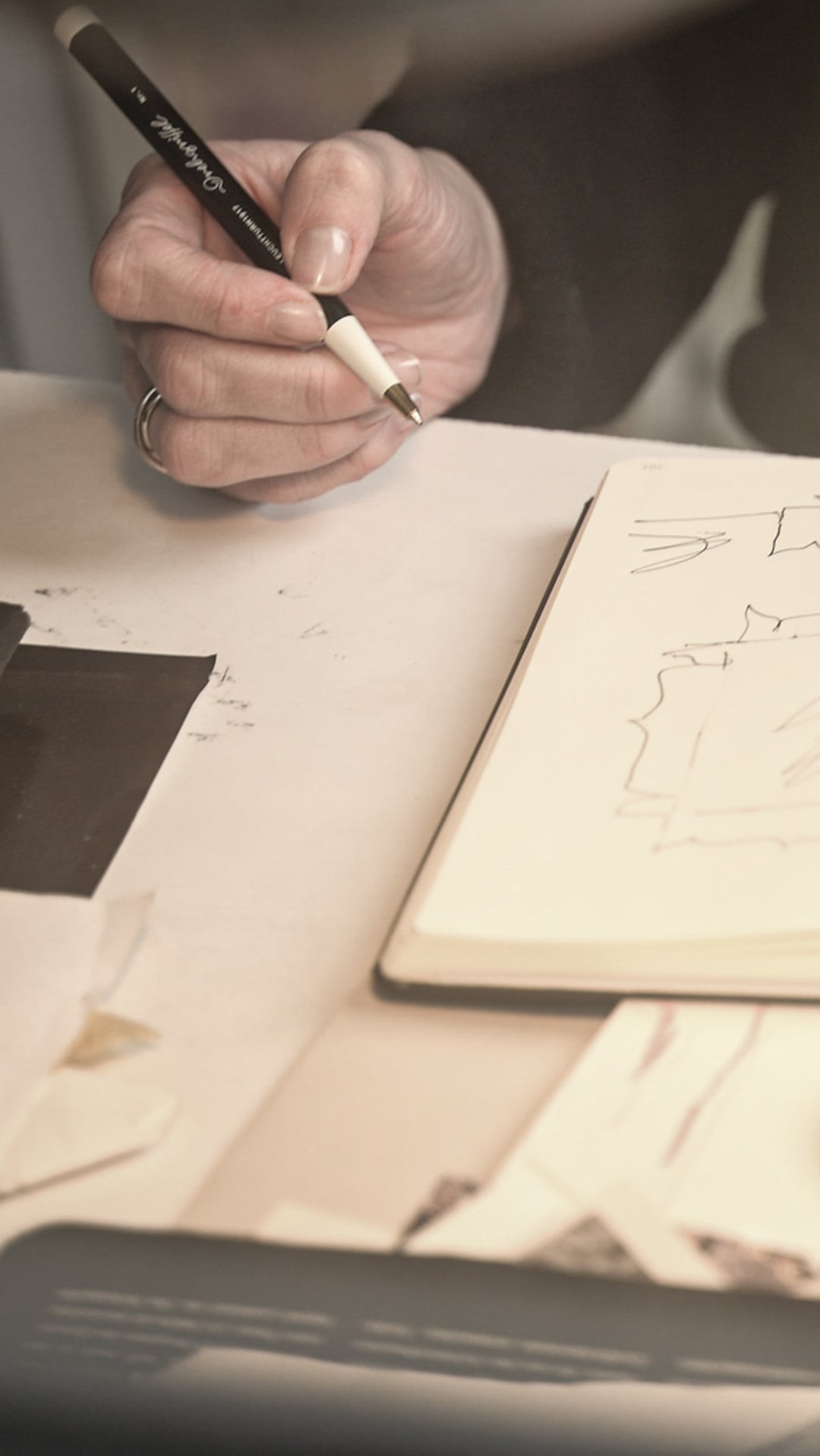Person drawing in a notebook with a pen on a desk.
