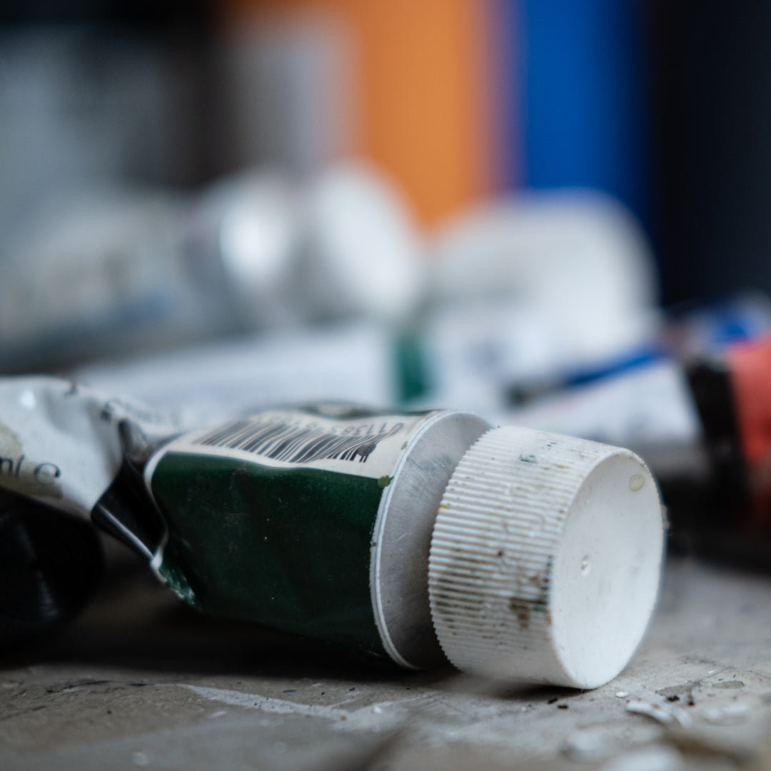Close-up of a used paint tube with blurred paint cans in the background