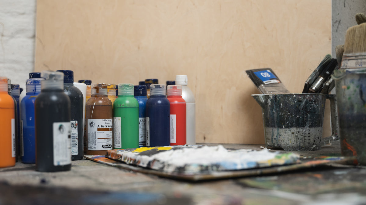 Art supplies including bottles of paint and a palette on a wooden surface.