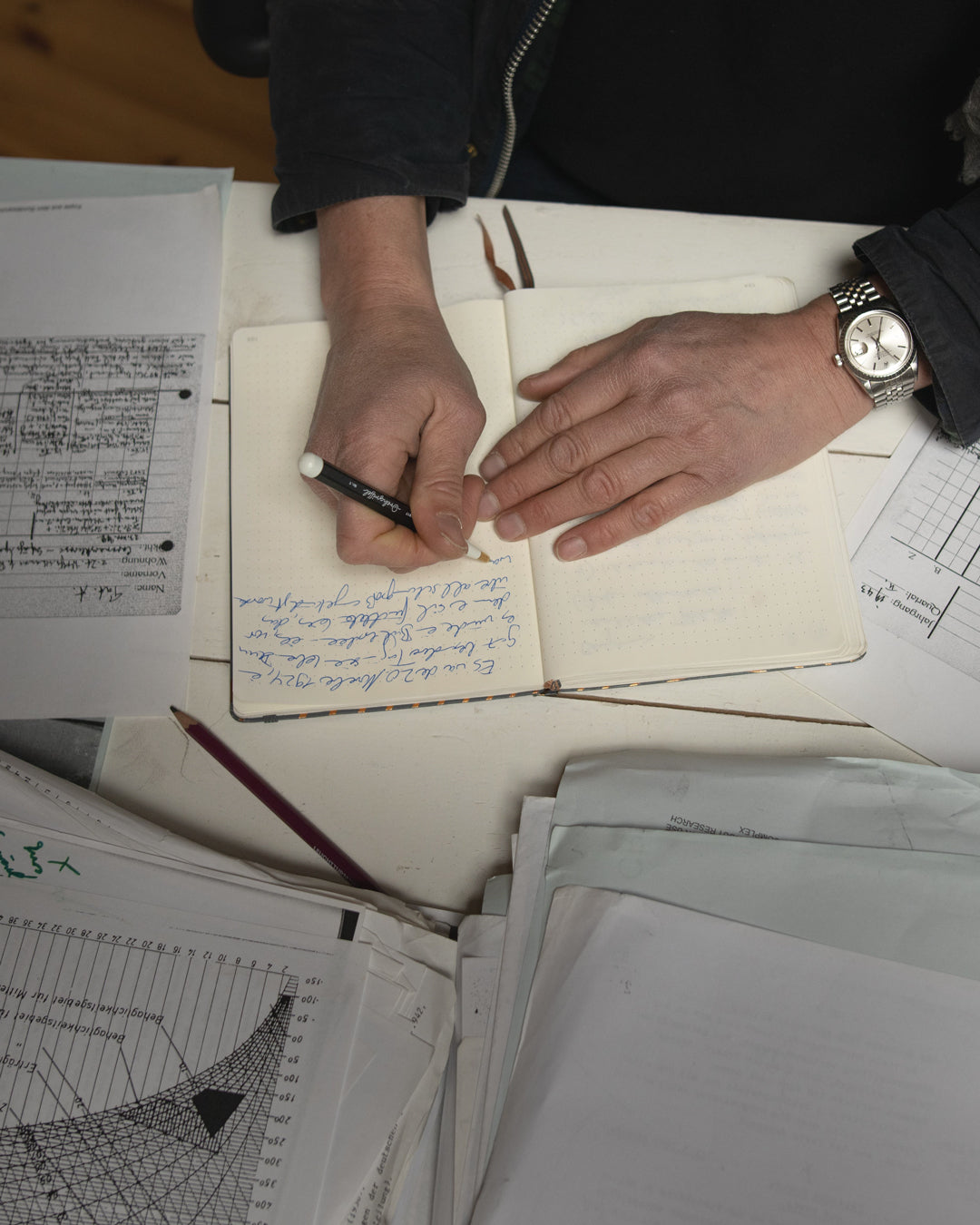 Person writing in a notebook with papers scattered around