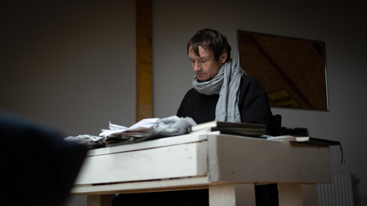 Man sitting at a desk in a dimly lit room with a scarf around his neck.