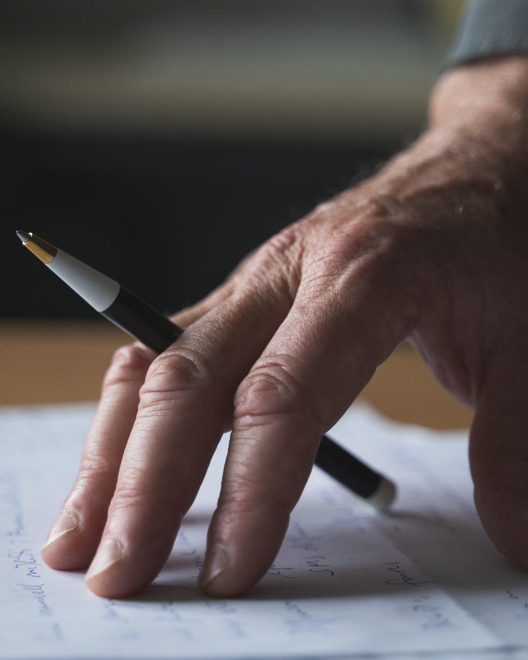 Hand holding a pen over a piece of paper with a blurred background