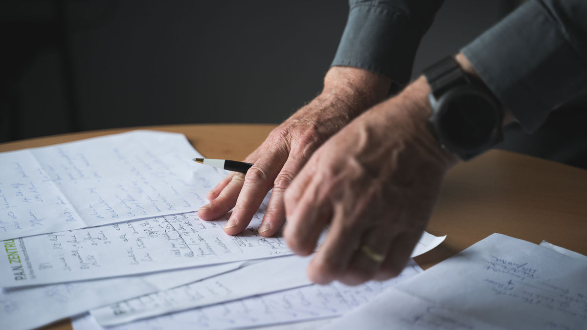 Close-up of hands on a document with a pen, on a wooden table.