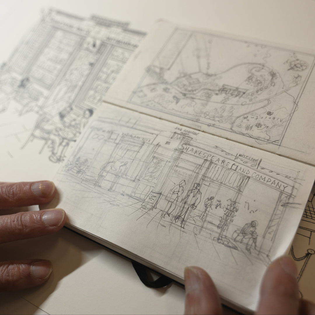 Hand holding a small notebook with black and white illustrations of a store front.