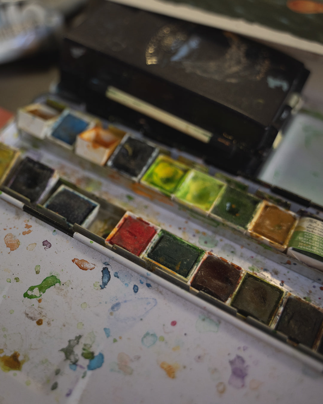 Set of watercolor paints with a paintbrush on a surface with paint splashes