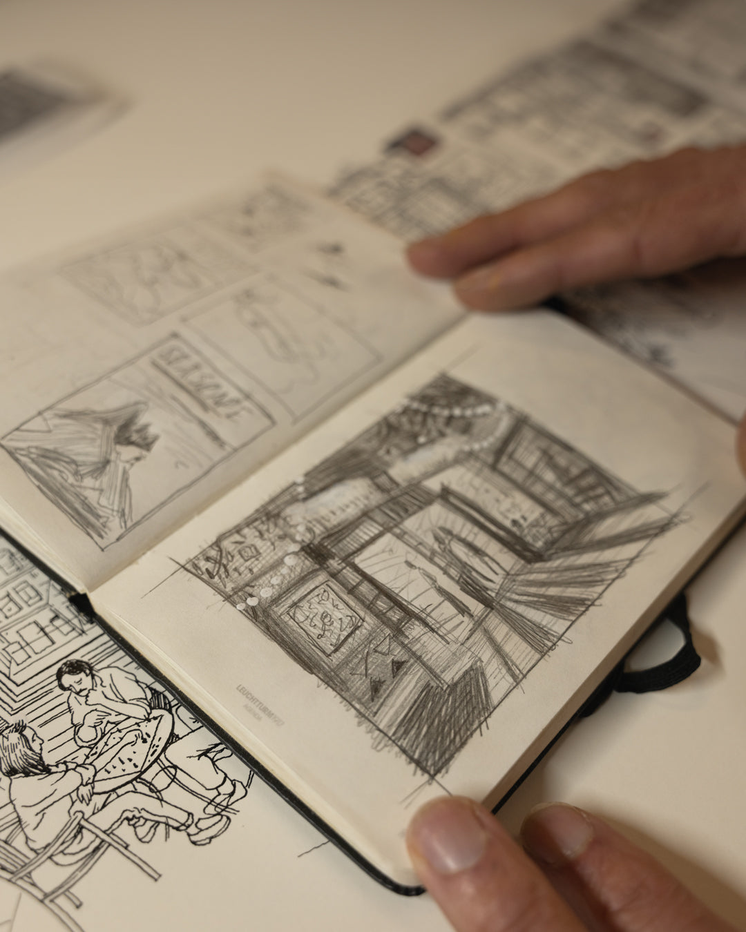 Open sketchbook with black and white illustrations of scenes, held by a person's hand.