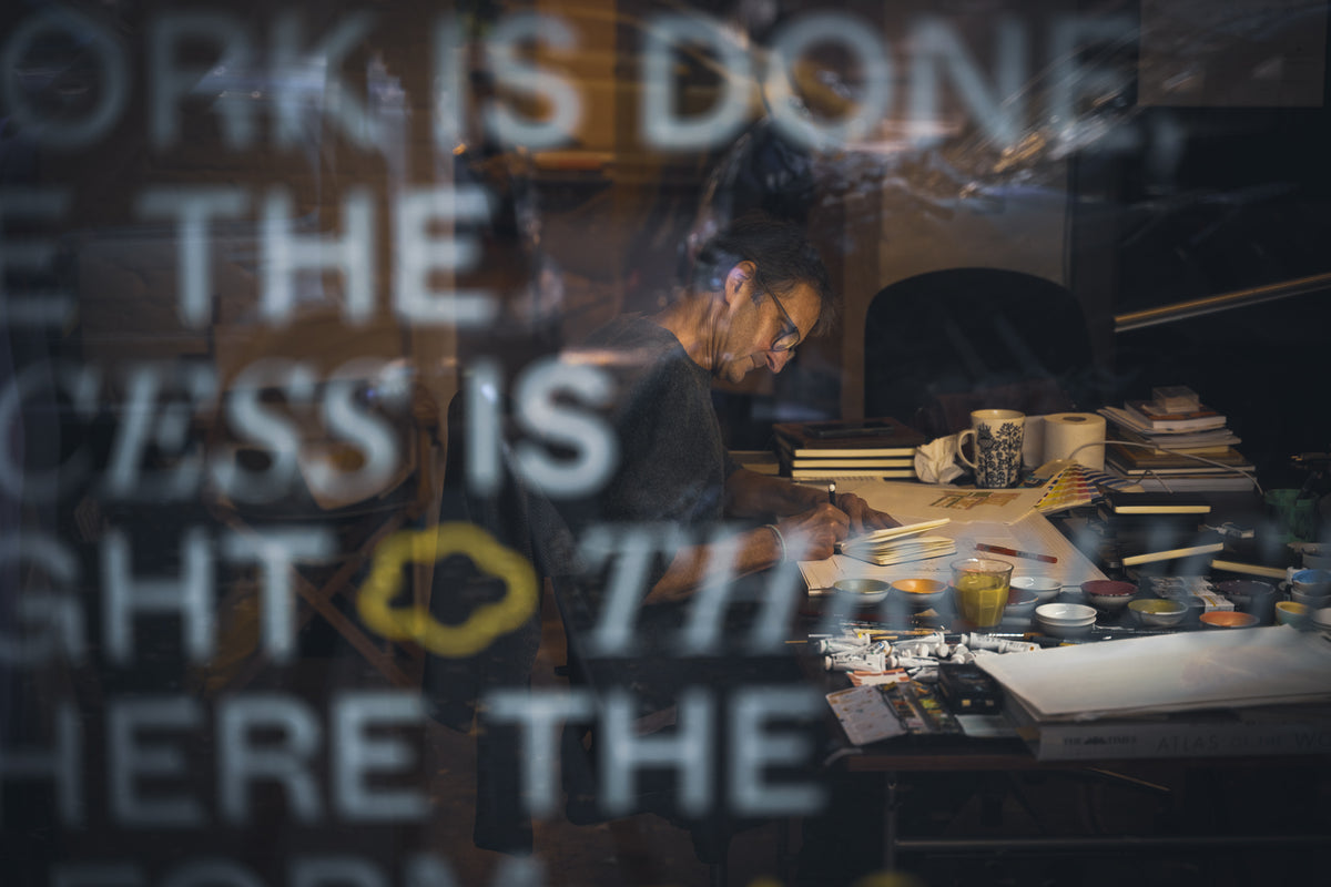 Looking through the window at a man sitting at desk writing in a notebook