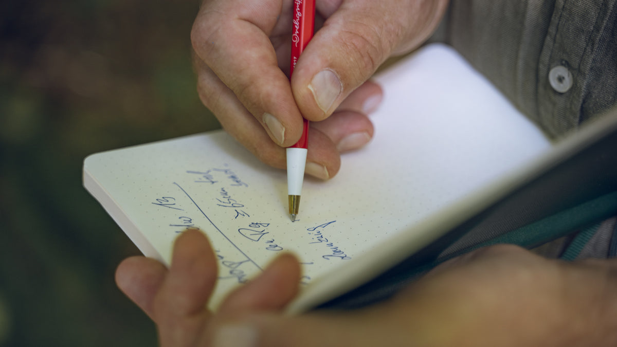 Person writing in a notebook with a red pen.