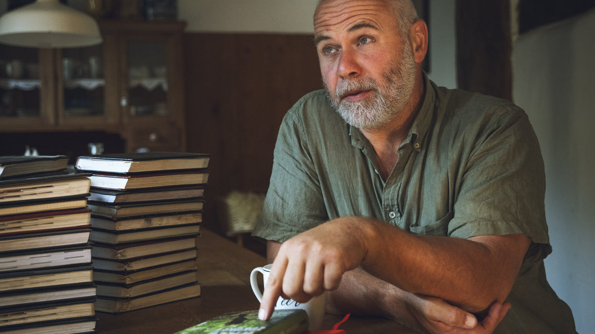 Man sitting at a table with books and a cup, in a home setting.