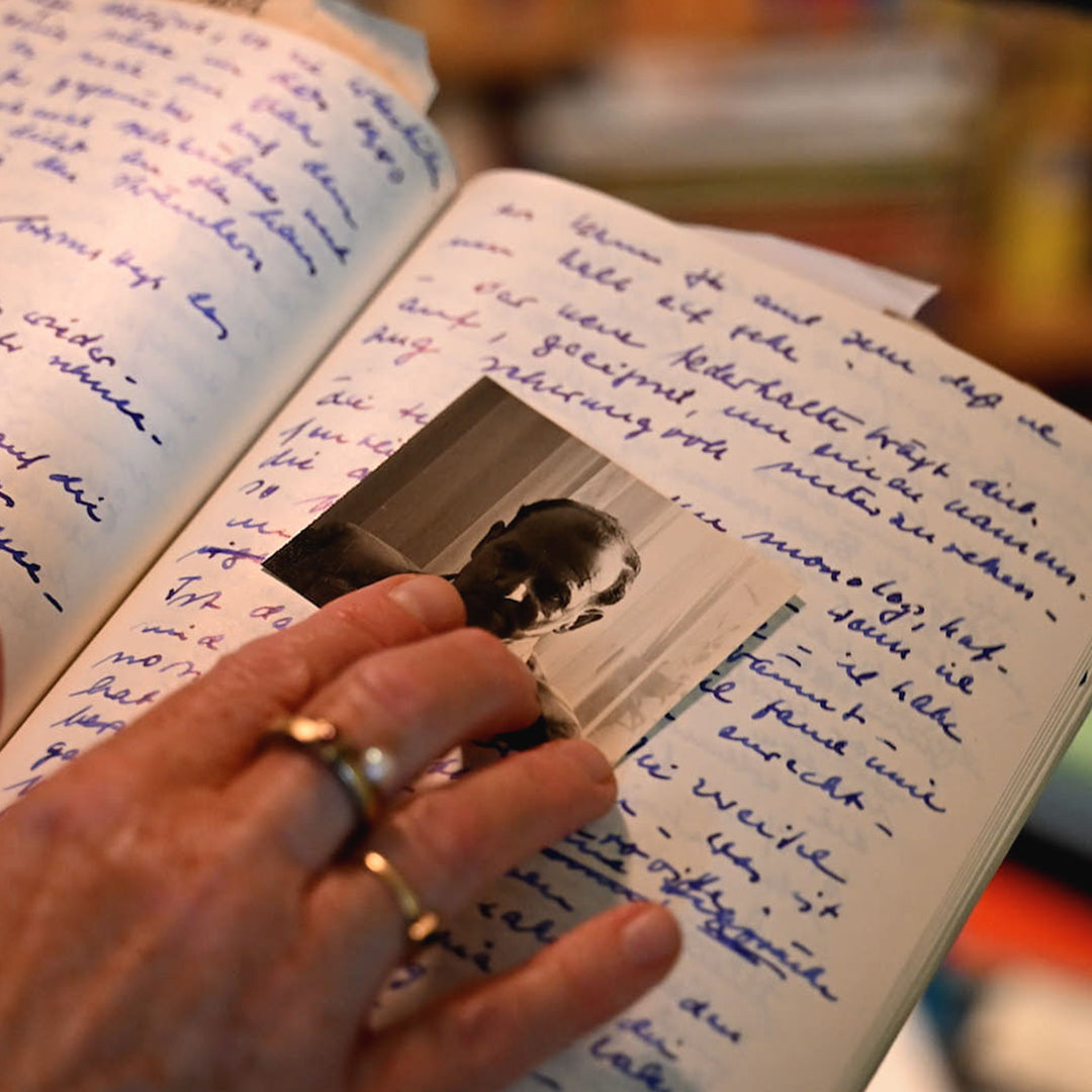 Hand holding a small photo of a man inside an open book with handwritten text.