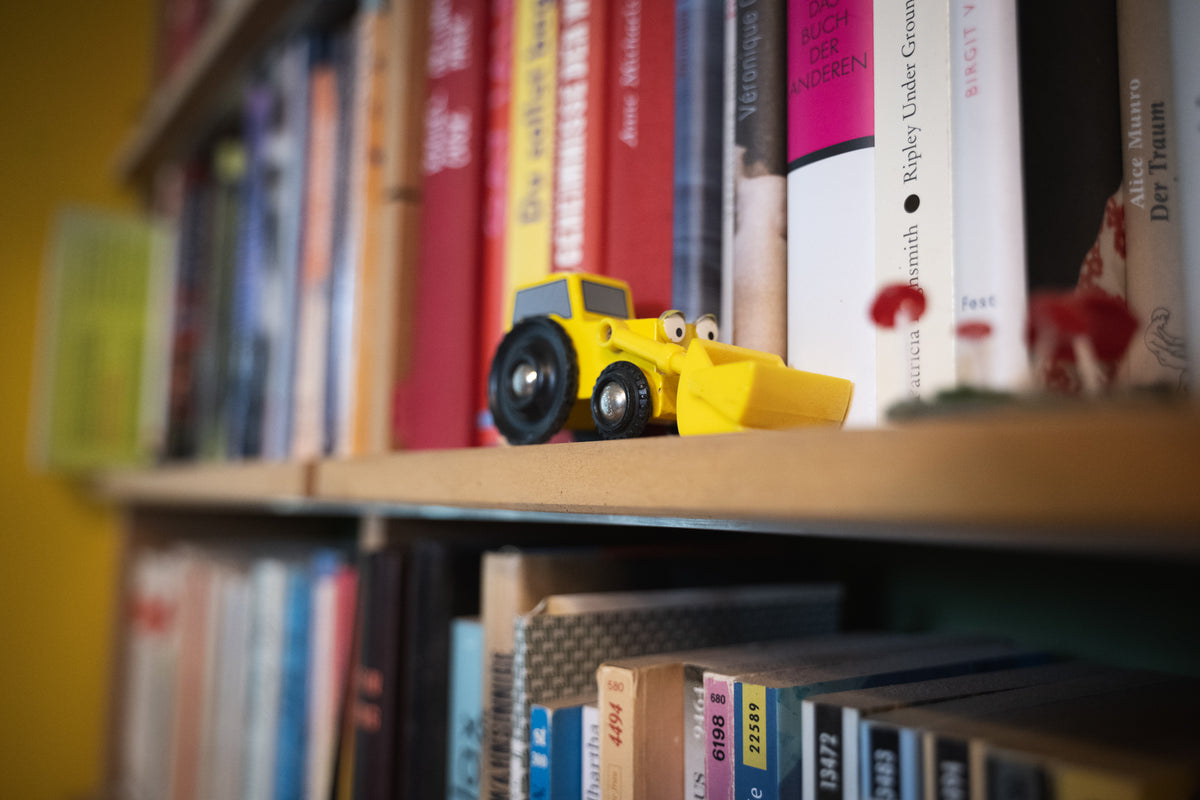 Toy bulldozer on a bookshelf with books in the background
