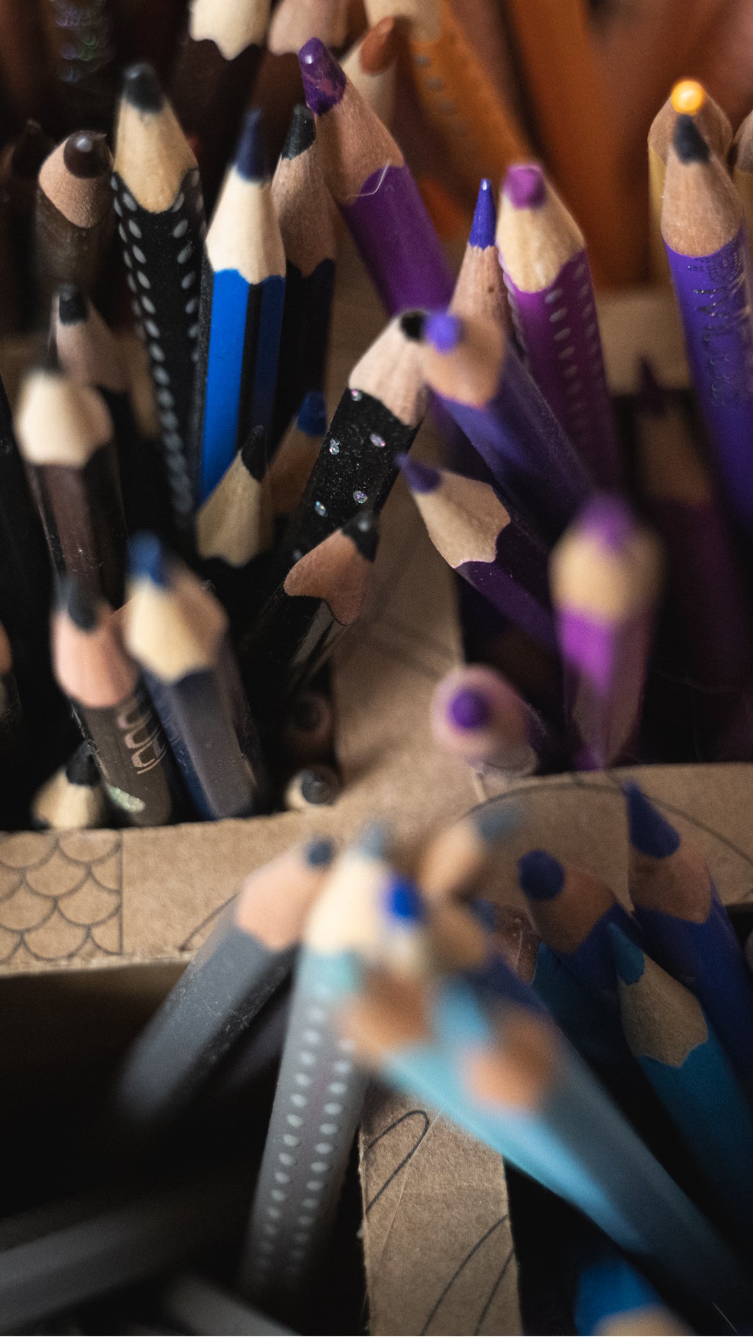 Collection of colored pencils with purple and blue accents in a box.