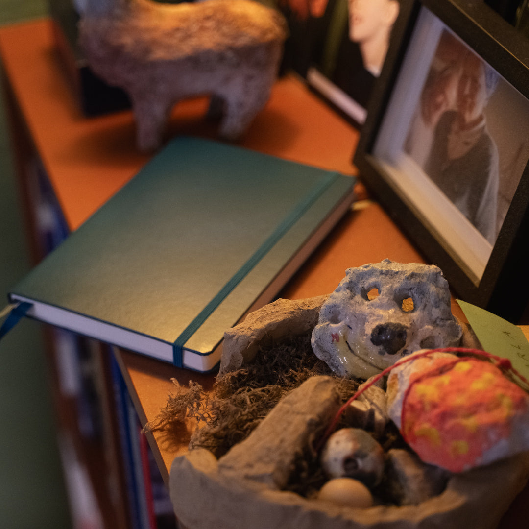 Small stuffed animal in a nest on a table with a notebook and photo frame in the background