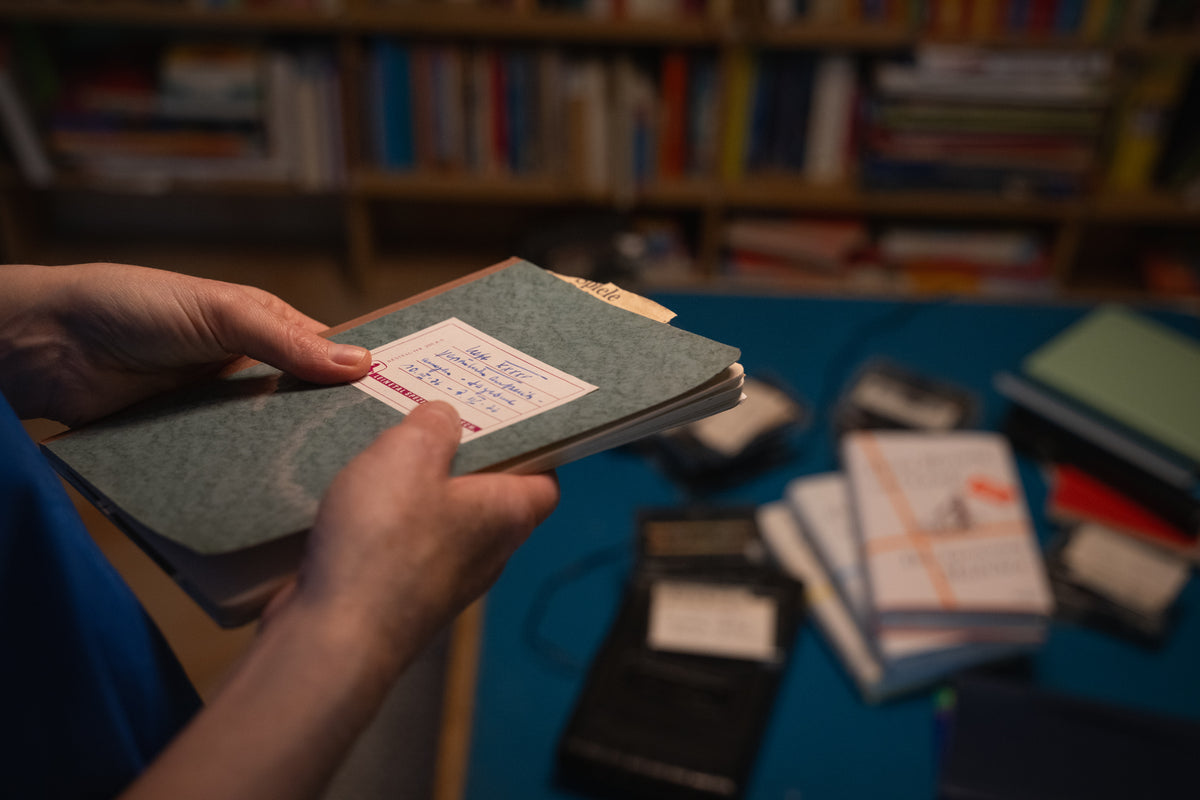 Person holding a small book with a colorful illustration in a room filled with books.